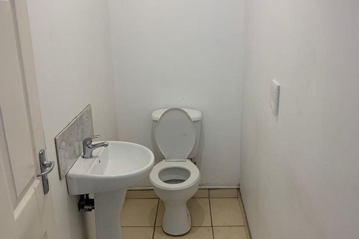 A compact, functional bathroom featuring a pedestal basin and toilet with neutral tiled flooring and plain white walls.