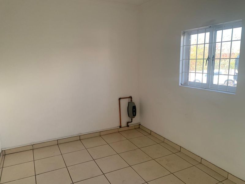 A vacant utility space featuring tiled flooring, a window with security bars, and an installed electric water heater with exposed plumbing.
