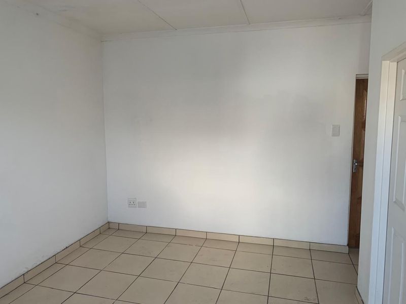 An empty, neutral-toned room featuring tiled flooring, standard electrical fixtures, and a timber door, suitable for various industrial or office uses.