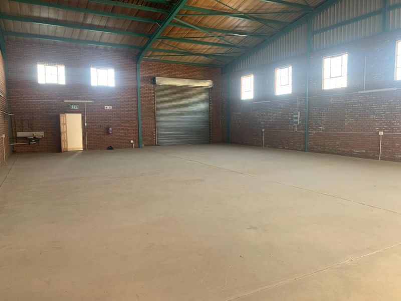 Spacious industrial warehouse unit featuring exposed brick walls, high steel truss ceilings, concrete flooring, and a large roller shutter door for easy access.