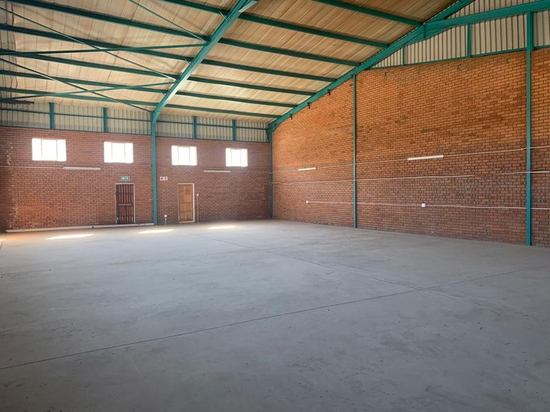 Spacious industrial warehouse unit featuring high ceilings with exposed steel trusses, durable concrete flooring, and exposed brick walls.