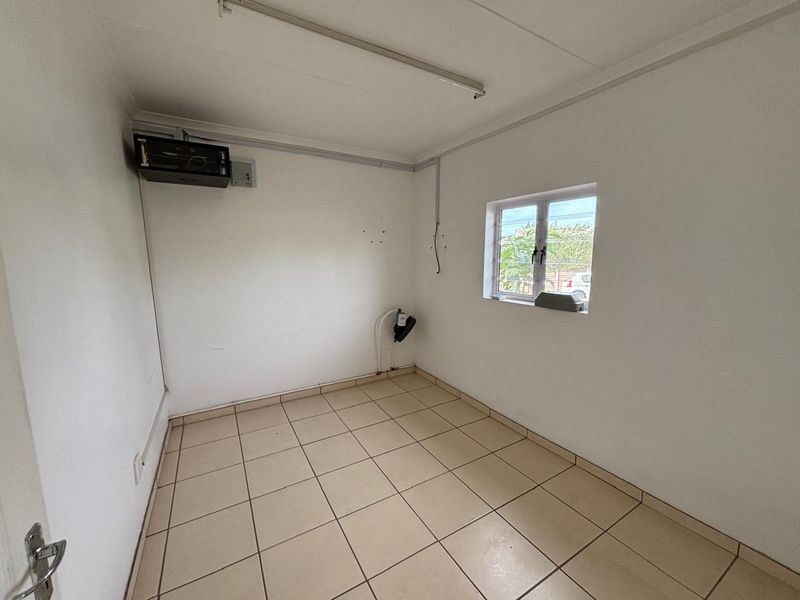 A functional, empty utility space featuring tiled flooring, a window, and exposed electrical conduit, suitable for various industrial or storage purposes.