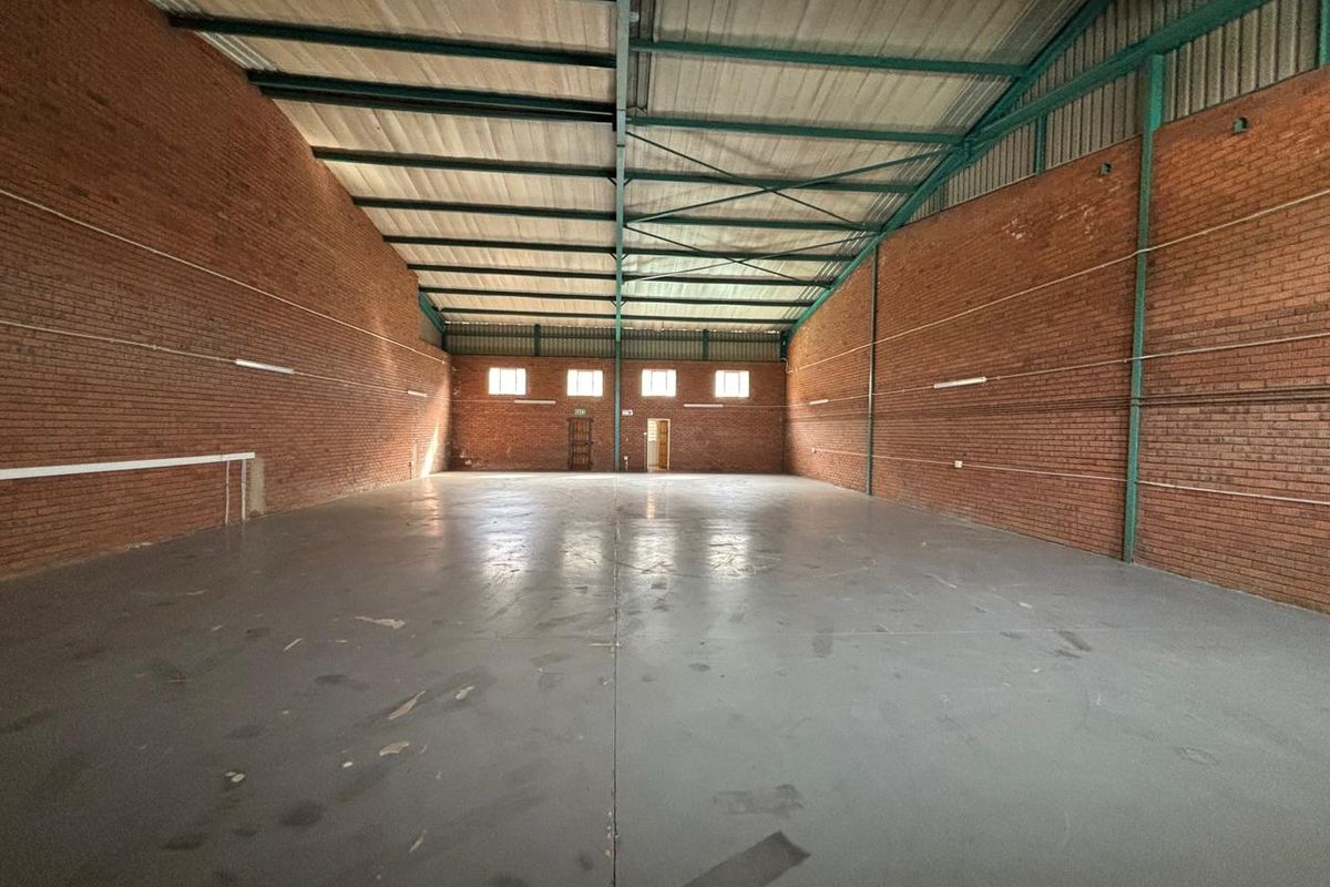 Spacious industrial warehouse unit featuring exposed brick walls, high steel truss ceilings, and durable concrete flooring, suitable for storage or manufacturing operations.