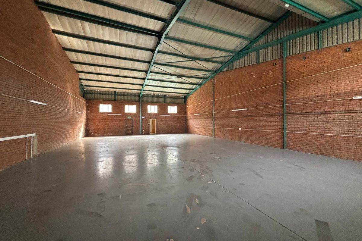 Spacious industrial warehouse unit featuring exposed brick walls, high-clearance steel portal frame, concrete flooring, and functional strip lighting.