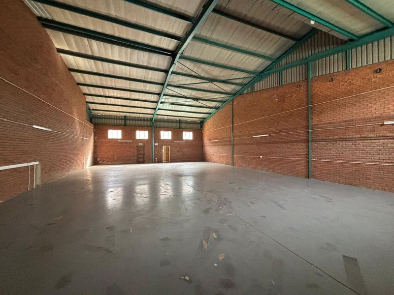 Spacious industrial warehouse unit featuring exposed brick walls, high-clearance steel portal frame, concrete flooring, and functional strip lighting.