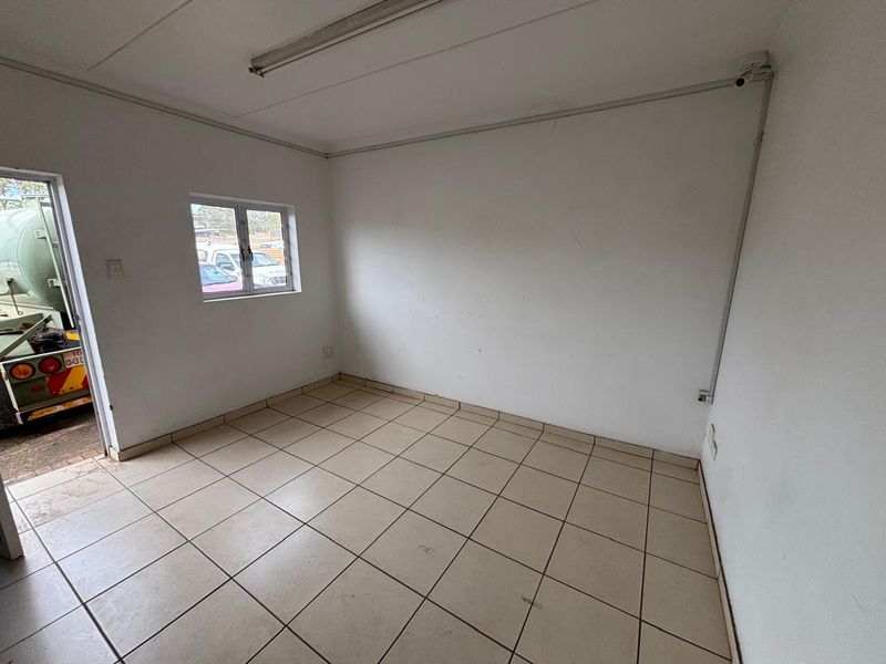 A vacant, functional office space featuring tiled flooring, surface-mounted electrical conduits, and a security camera, suitable for industrial or commercial use.