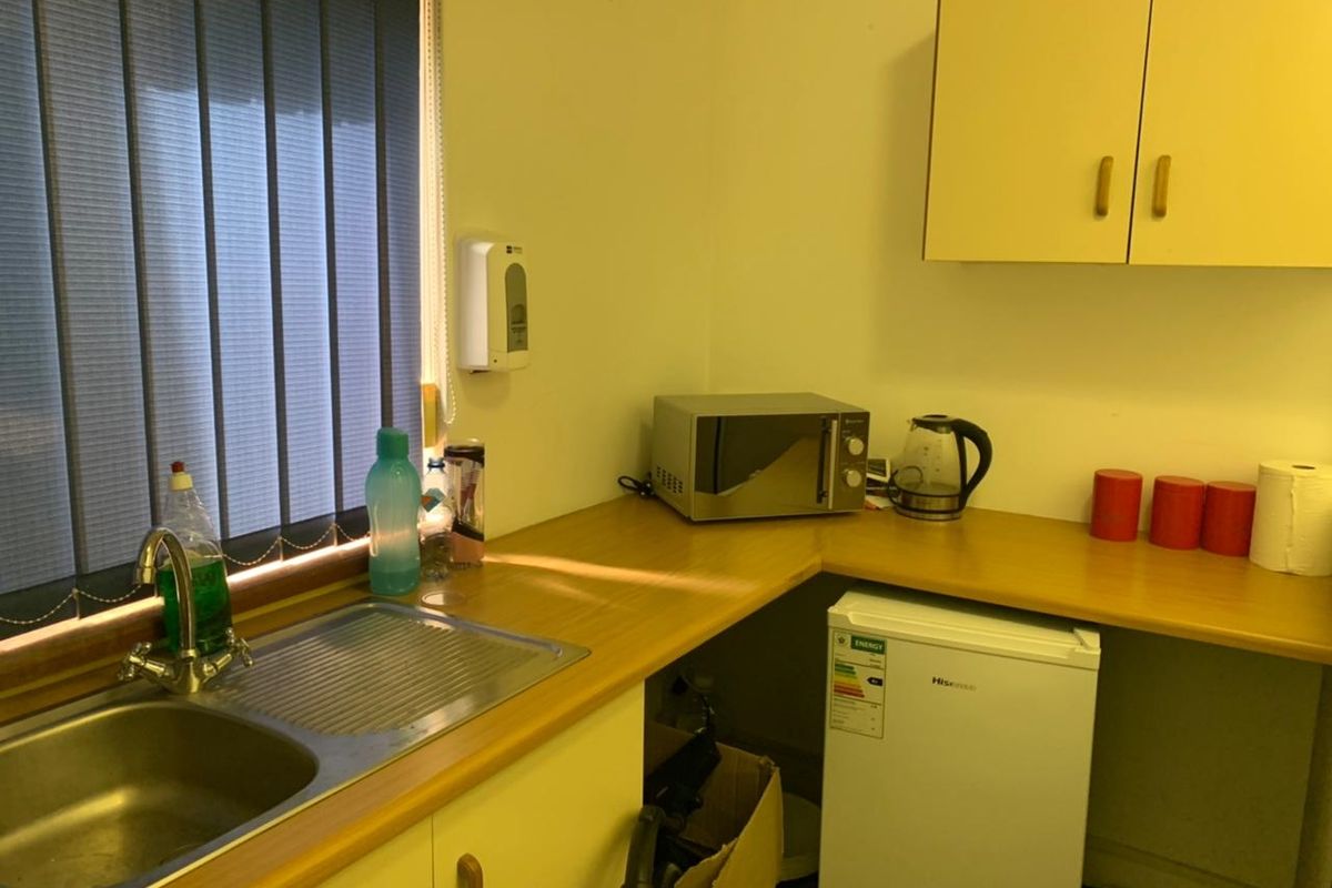 A compact office kitchenette featuring laminate countertops, stainless steel sink, and wall-mounted storage cabinetry.