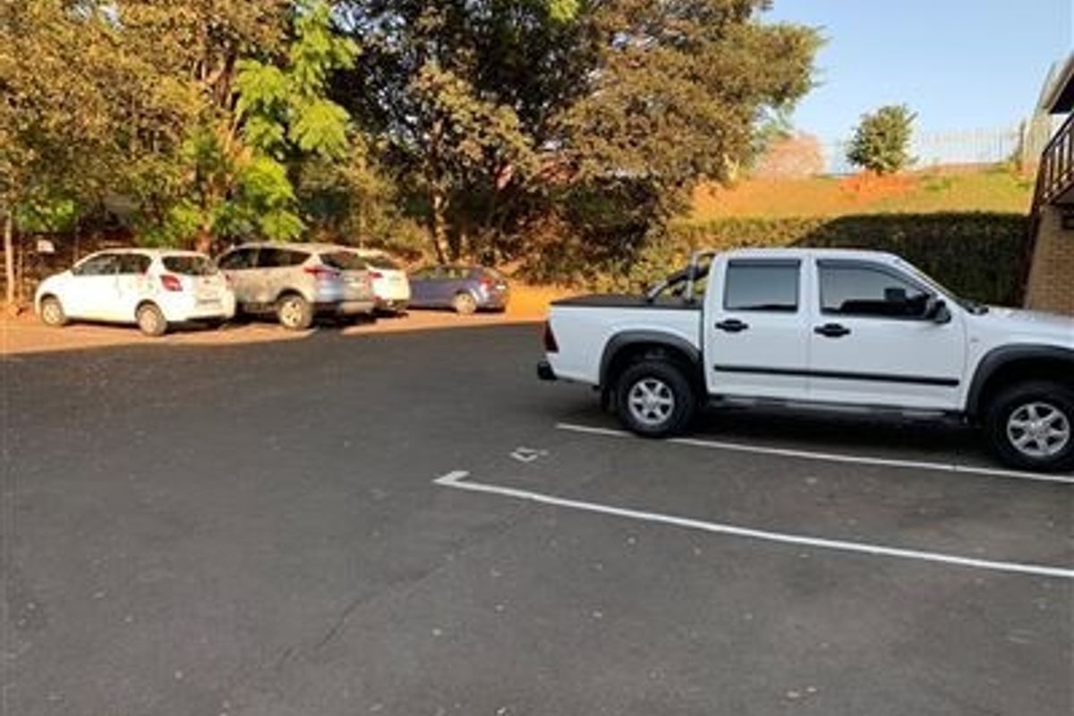 An outdoor asphalt parking area with marked bays, situated adjacent to the office building with surrounding trees.