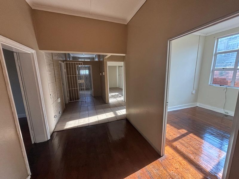 A view of an office interior featuring polished wooden floors, tiled transition areas, and multiple doorways leading to connected workspaces.