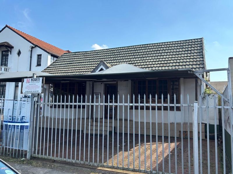Front exterior view of a commercial office property featuring a tiled roof, security fencing, and a paved entrance area.