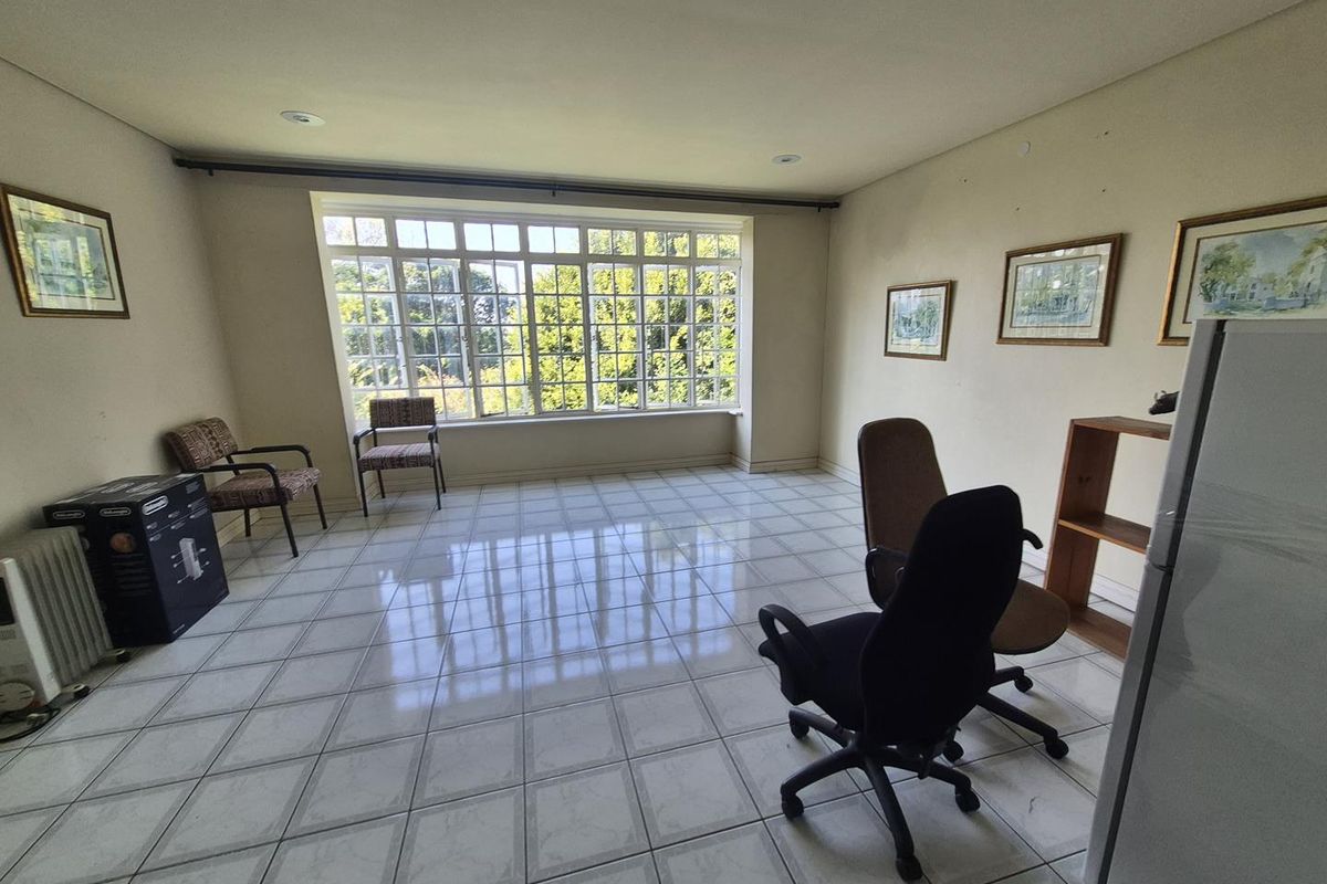 A spacious, light-filled room featuring large multi-pane windows, tiled flooring, and recessed ceiling lighting, suitable for use as a living area or home office.