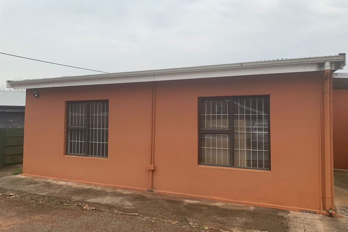 Rear exterior view of the office building featuring painted masonry walls, security-barred windows, and a concrete perimeter apron.