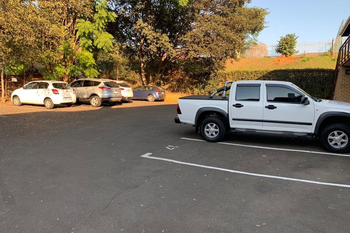 An outdoor paved parking area with marked bays, situated adjacent to the office building with surrounding trees and perimeter fencing.