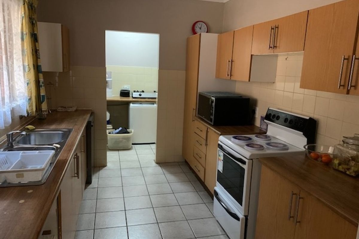 Functional kitchen featuring wood-look cabinetry, tiled flooring, and a tiled backsplash, with an adjoining scullery area for additional utility and appliance space.