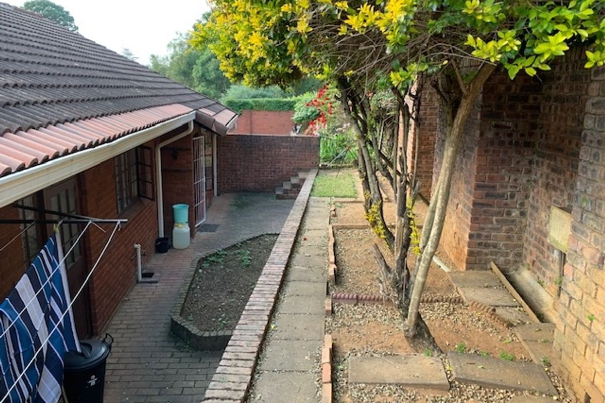 A private rear courtyard featuring brick boundary walls, paved pathways, and established garden beds alongside the townhouse exterior.
