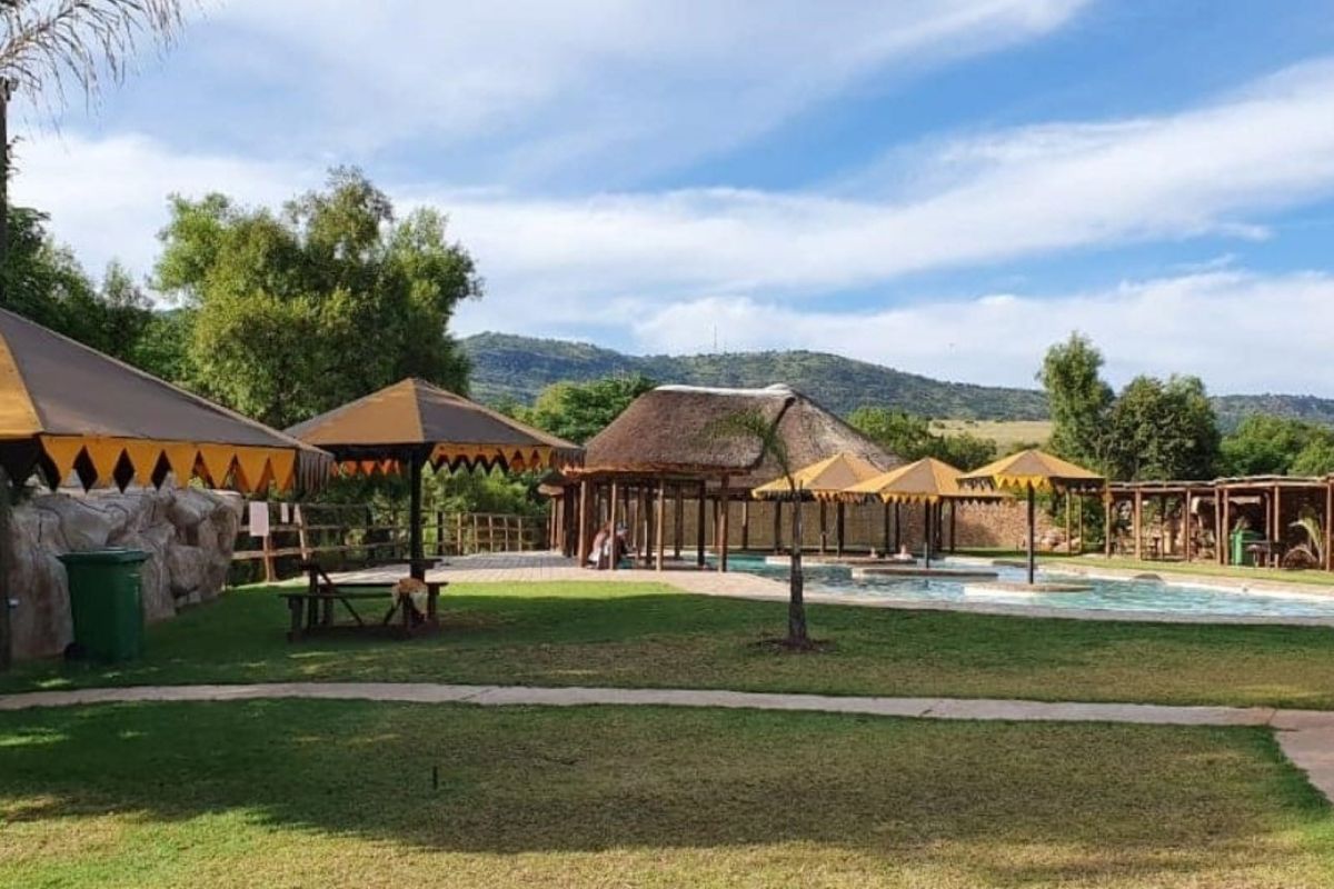Outdoor pool area featuring a swimming pool, thatched roof structures, and landscaped grounds with mountain views.