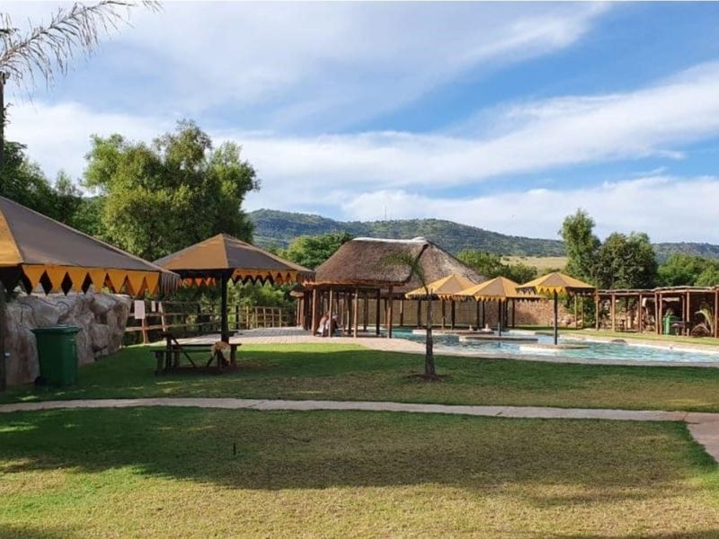 Outdoor pool area featuring a swimming pool, thatched roof structures, and landscaped grounds with mountain views.