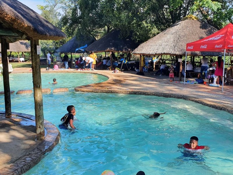 Outdoor pool area featuring multiple thatched lapa structures and paved surrounds, providing a recreational space for guests.