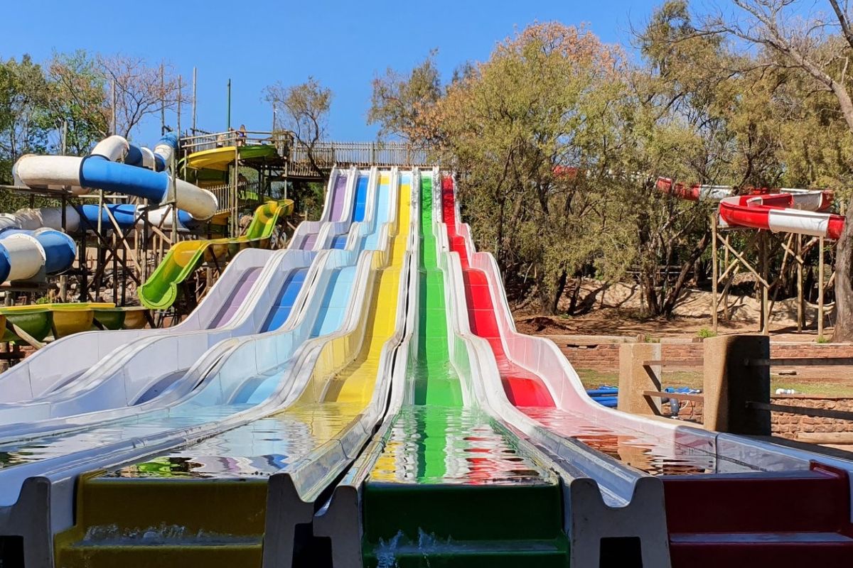 A multi-lane outdoor water slide facility featuring vibrant colored tracks and integrated water flow system set within a landscaped park environment.