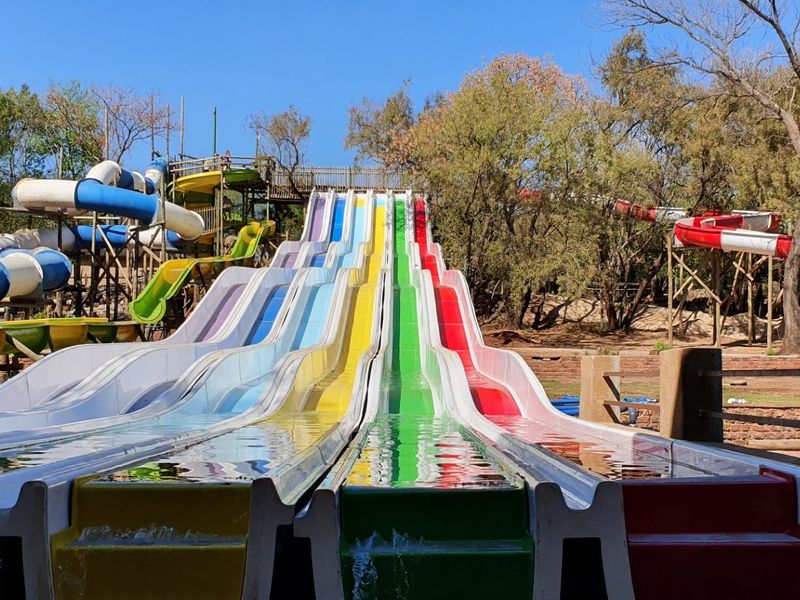 A multi-lane outdoor water slide facility featuring vibrant colored tracks and integrated water flow system set within a landscaped park environment.