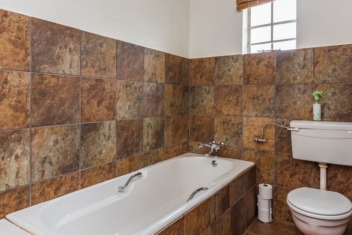 A functional bathroom featuring a built-in bathtub with chrome fixtures and a standard toilet, finished with full-height rustic-style wall tiling.