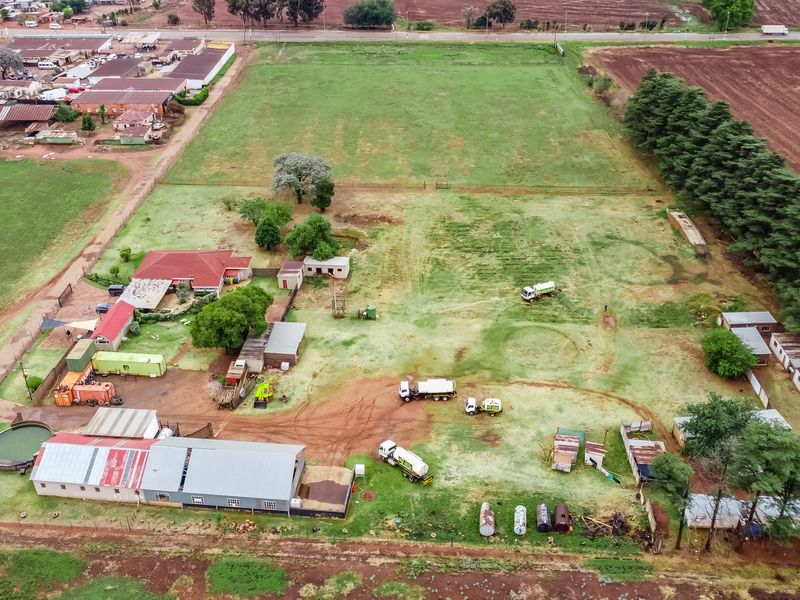 Aerial view of a small holding property featuring a main dwelling, multiple outbuildings, large open land, and water storage infrastructure.