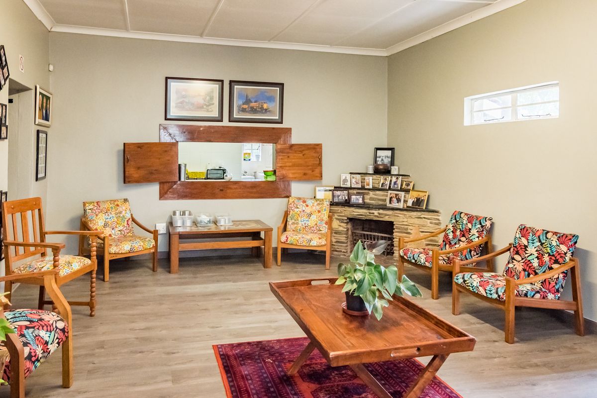A spacious living room featuring a stone fireplace, laminate flooring, and a unique wooden-shuttered serving hatch connecting to the kitchen area.