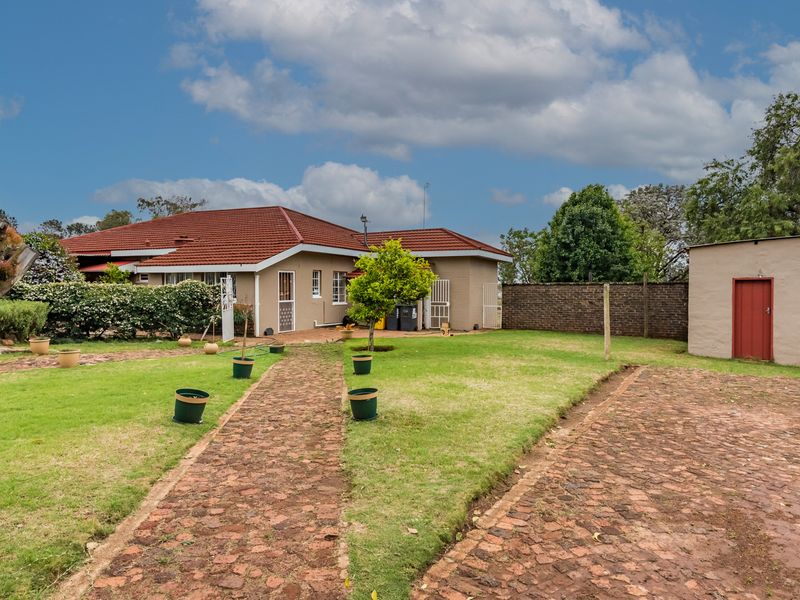Rear view of the property featuring a spacious garden, cobblestone pathways, a tiled roof dwelling, and a separate outbuilding with a secure entrance.