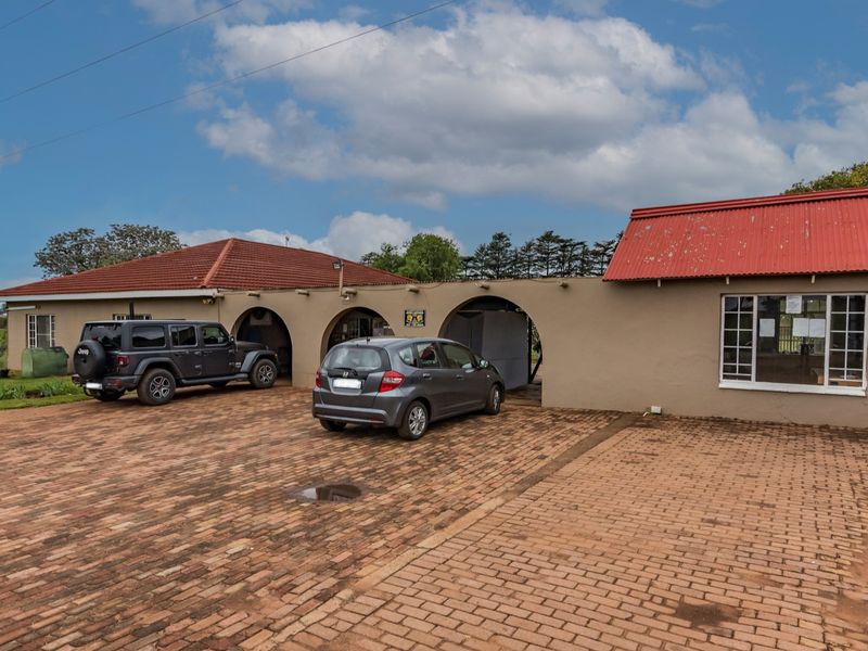 Front exterior view of a small holding property featuring a brick paved driveway, arched parking bays, and a combination of tiled and corrugated metal roofing.