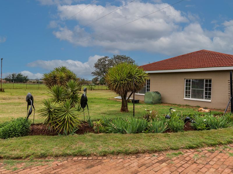 Rear view of the property featuring a tiled roof, security-barred windows, and a well-maintained garden area with brick paving.