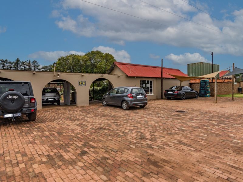 Front exterior view of the property featuring a large brick-paved driveway, an arched carport structure, and a corrugated metal roof.