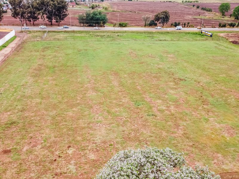 An aerial view of a large, open plot of land featuring established perimeter fencing and surrounding road access.