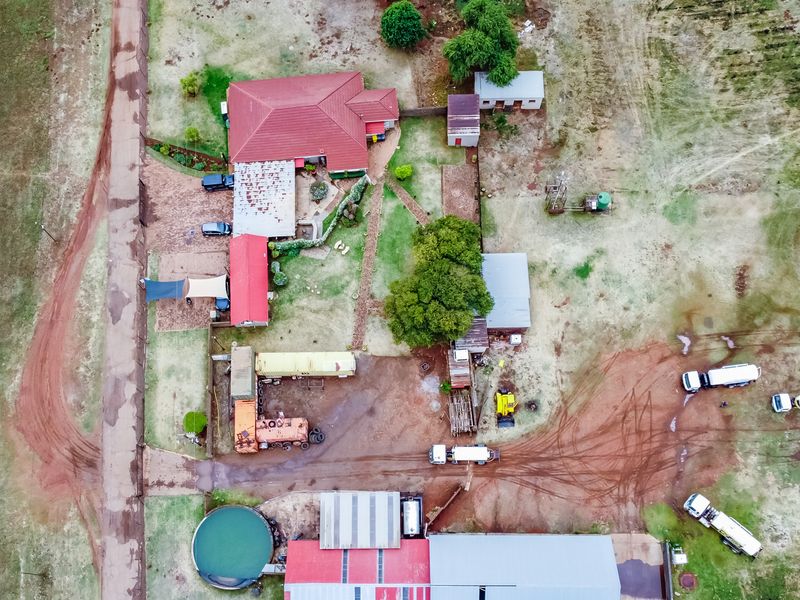 Aerial view of a small holding property featuring a main residence, multiple outbuildings, water storage infrastructure, and extensive open land with gravel access paths.