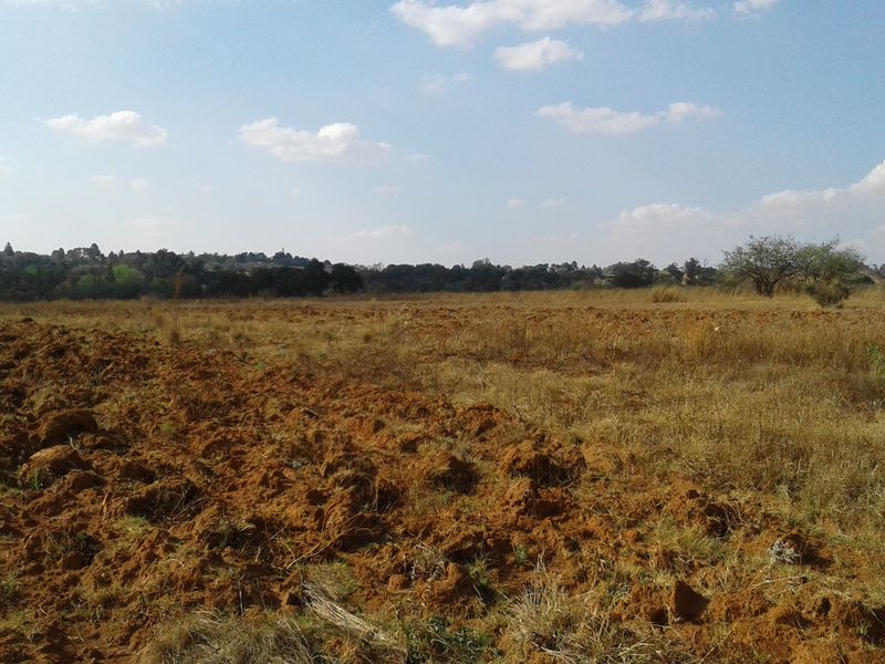 A view of a large, undeveloped commercial land plot featuring cleared soil and natural vegetation under a clear sky.