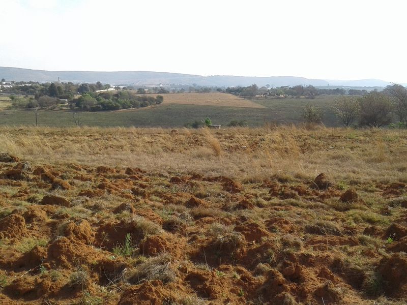 A wide-angle view of an expansive, undeveloped commercial land plot featuring natural terrain and distant landscape vistas.