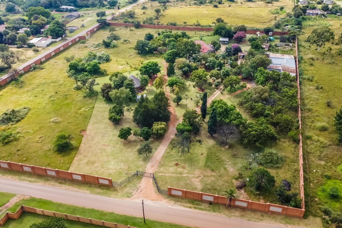 Aerial view of a large, enclosed commercial vacant land plot featuring mature trees, a gated entrance, and a perimeter brick wall.