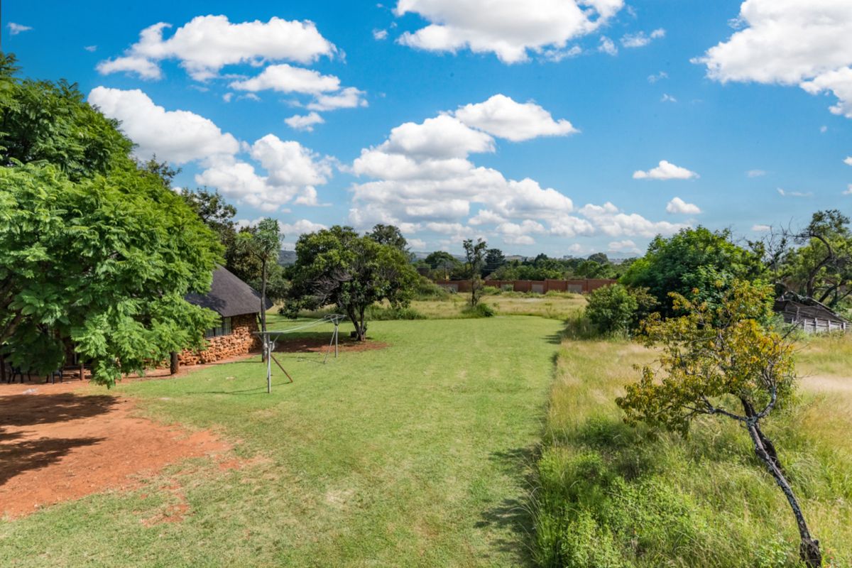 A view of the rear garden area featuring a stone-walled structure with a thatched roof, expansive lawn, and perimeter boundary wall.