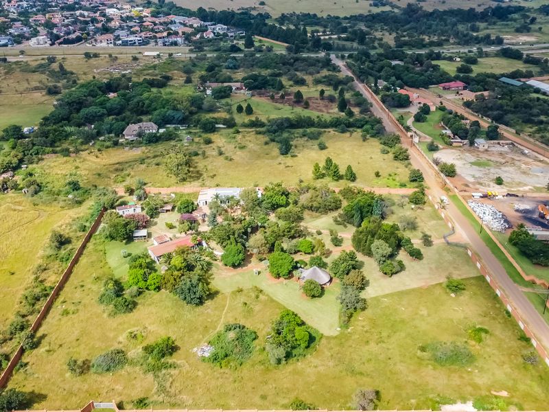 Aerial view of a large commercial vacant land plot featuring established trees, perimeter fencing, and existing structures with road access.