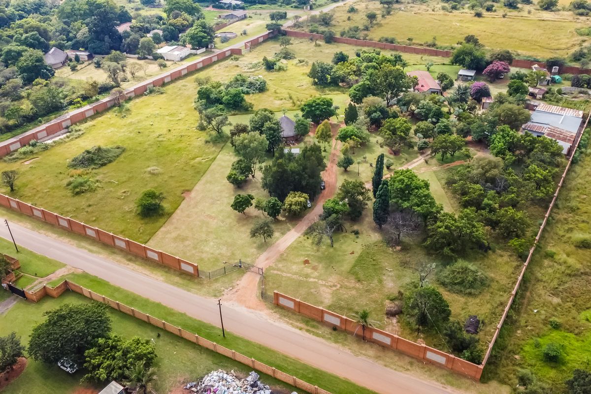 Aerial view of a large, enclosed commercial vacant land plot featuring mature trees, established perimeter walling, and existing outbuildings.