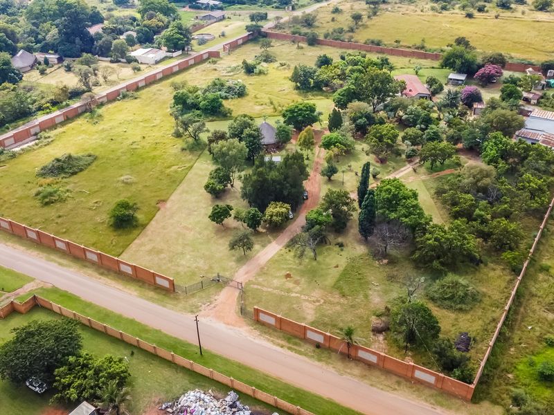 Aerial view of a large, enclosed commercial vacant land plot featuring mature trees, established perimeter walling, and existing outbuildings.