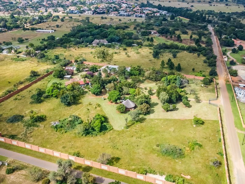 Aerial view of a large commercial vacant land plot featuring established trees, perimeter walling, and direct access to a paved road.
