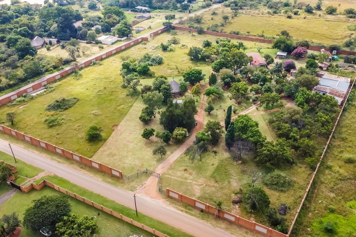 Aerial view of a large, expansive commercial vacant land plot featuring perimeter walling, established trees, and a gravel access driveway.