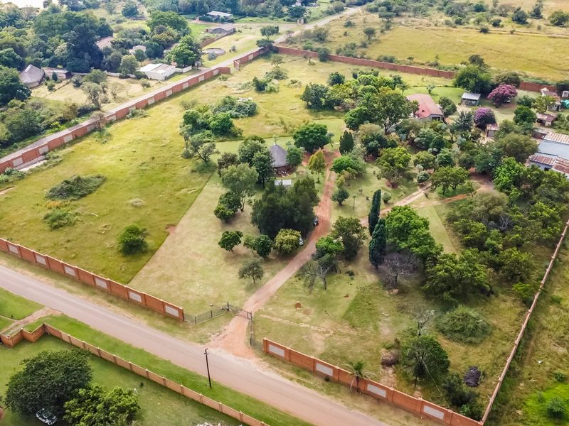 Aerial view of a large, expansive commercial vacant land plot featuring perimeter walling, established trees, and a gravel access driveway.