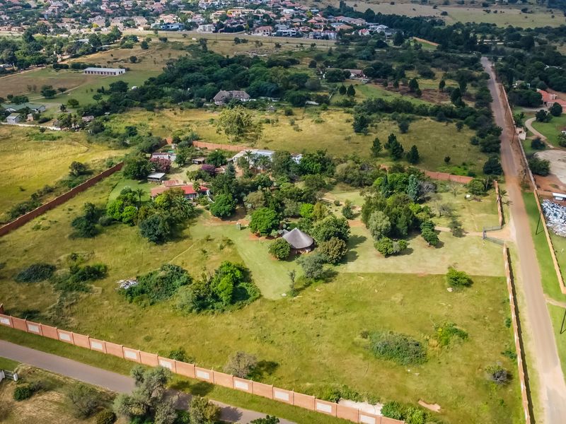 Aerial view of a large commercial vacant land plot featuring perimeter walling, established trees, and direct access to a public road.