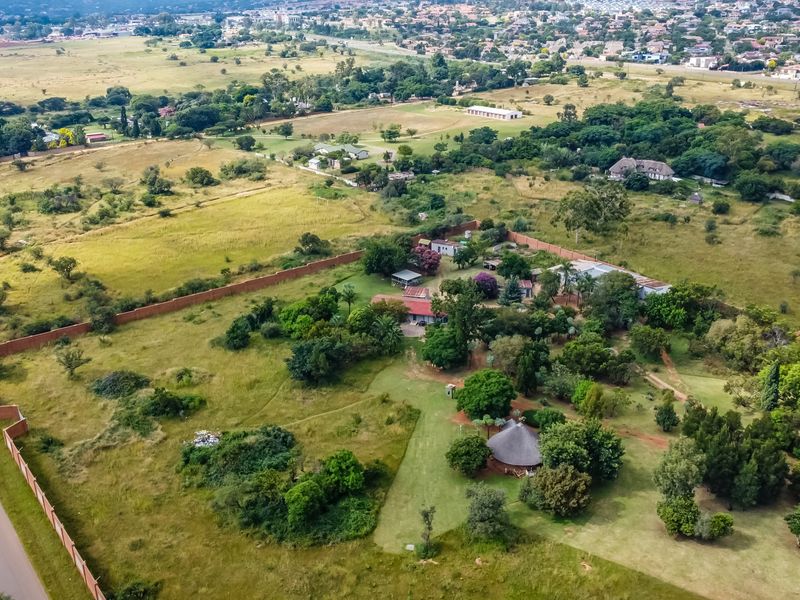 Aerial view of a large vacant commercial land plot featuring established trees, perimeter walling, and direct access to a public road.