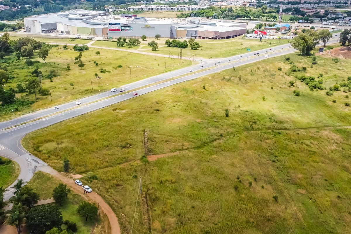 Aerial view of a large, undeveloped commercial land parcel situated adjacent to a major road and a large shopping center.