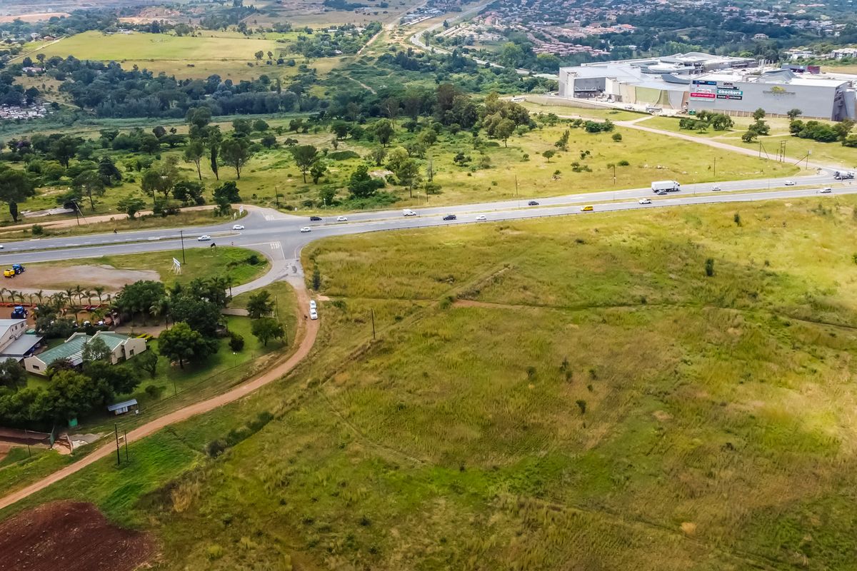 Aerial view of a large vacant commercial land parcel situated near a major road and established commercial shopping center.