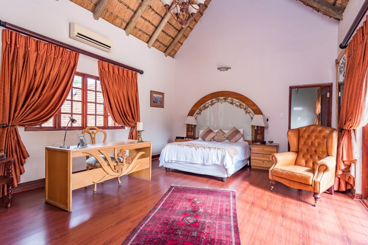 Spacious bedroom featuring a high vaulted thatched ceiling, laminate flooring, and a decorative built-in headboard with integrated bedside lighting.
