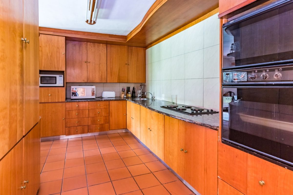 A functional kitchen featuring extensive wooden cabinetry, built-in wall ovens, a cooktop, and tiled flooring, offering a classic layout with ample storage space.