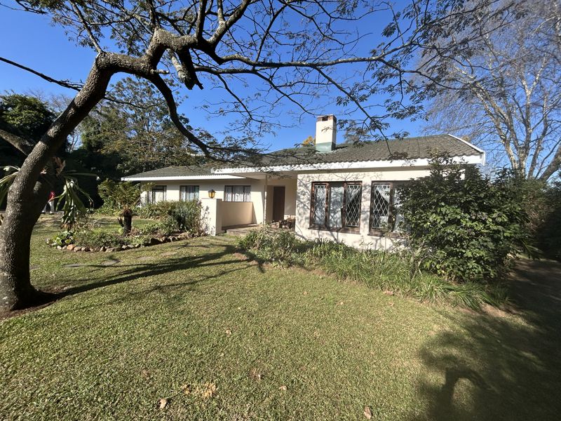 A single-story residential home featuring a tiled roof, chimney, and diamond-patterned windows, set within a mature garden with established trees.